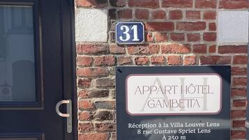 Paret de maó amb una porta i dos senyals: un indica el número 31 i l'altre per 'Appart Hotel Gambetta' amb recepció a Villa Louvre Lens.