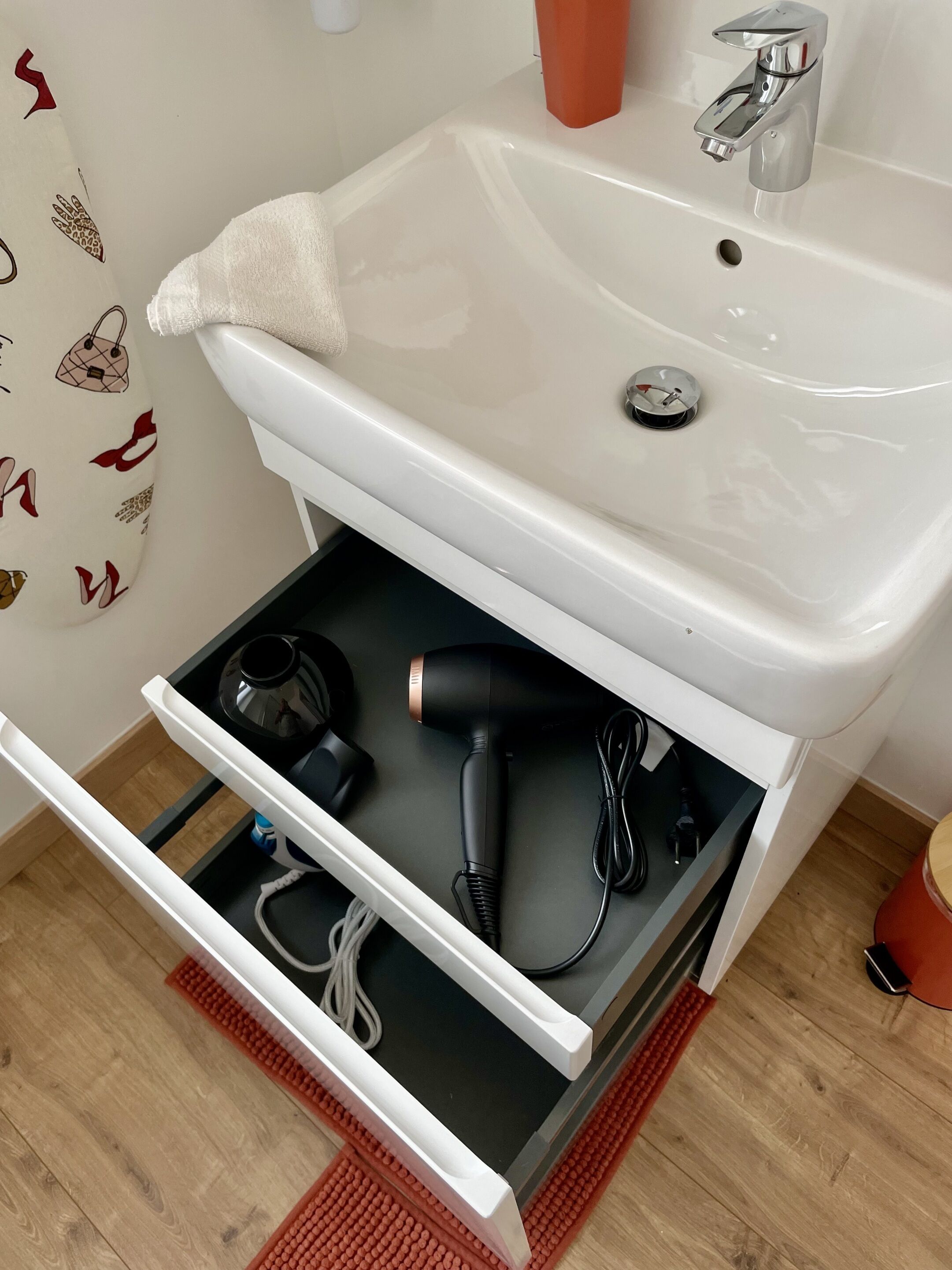 Un baño con lavamanos blanco, una toalla y un secador de pelo en un cajón.