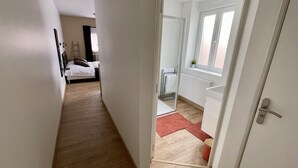 En smal hall som leder till ett sovrum med en säng, ett element och ett fönster.
