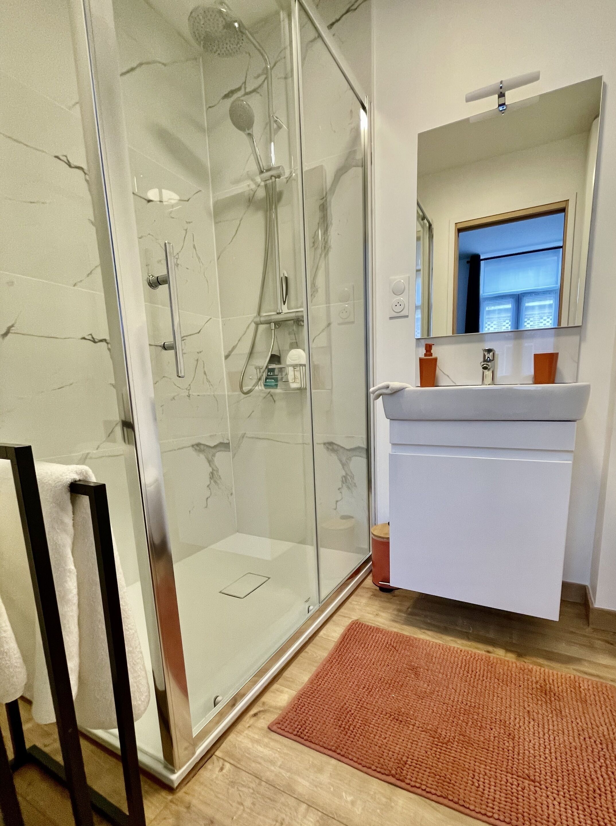 Une salle de bain moderne avec une douche à parois de verre, un lavabo blanc et un miroir au-dessus.