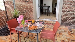 En uteplats med ett tegelgolv, ett bord dukat med mat och dryck samt ett rött parasoll.