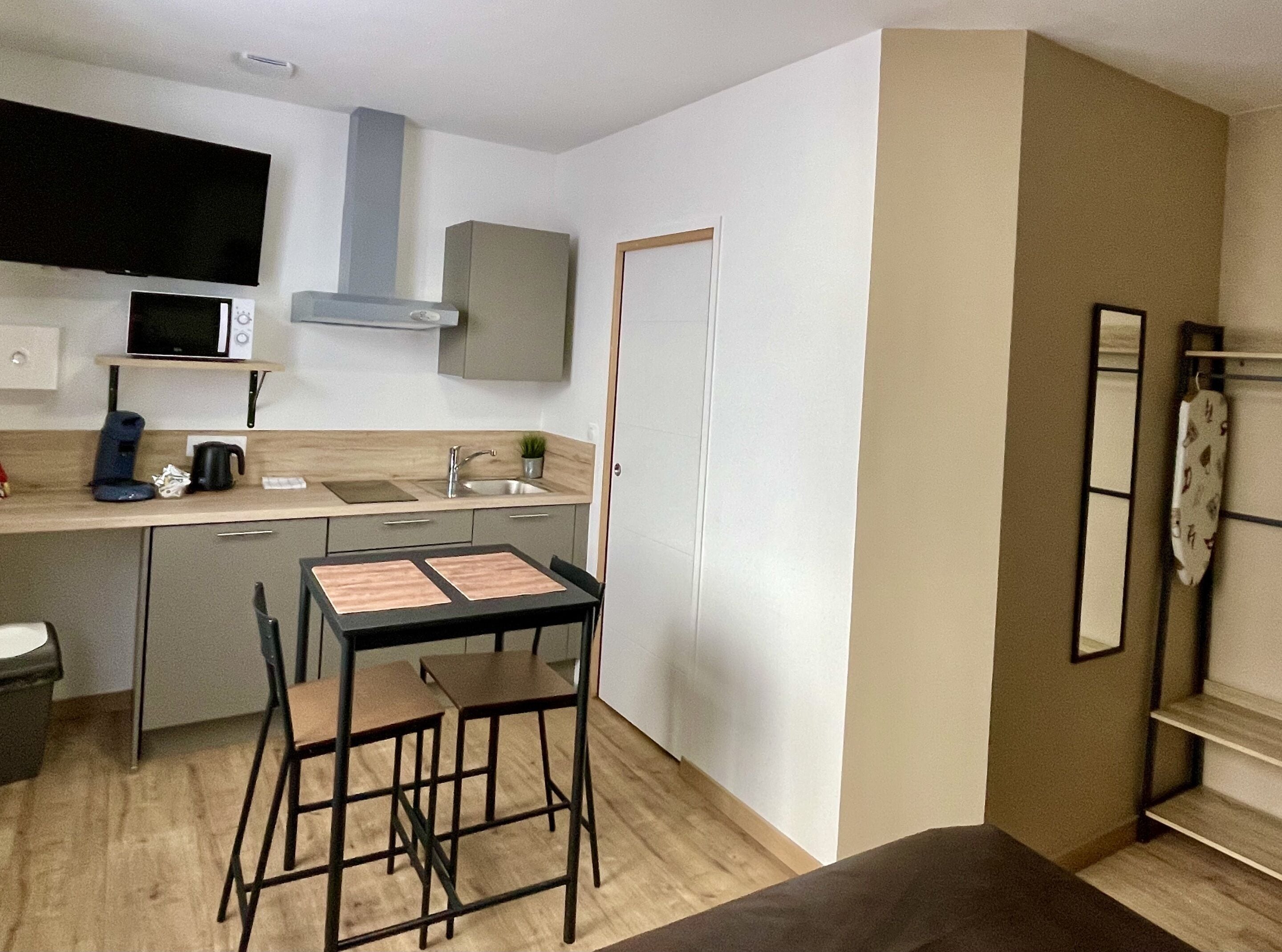 A compact kitchen with a microwave, sink, and stove, a small dining table with chairs, and a single door.