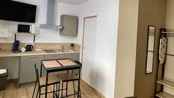 A compact kitchen with a microwave, sink, and stove, a small dining table with chairs, and a single door.