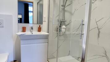 Une salle de bain moderne avec une douche à parois de verre, un lavabo blanc et un miroir au-dessus.