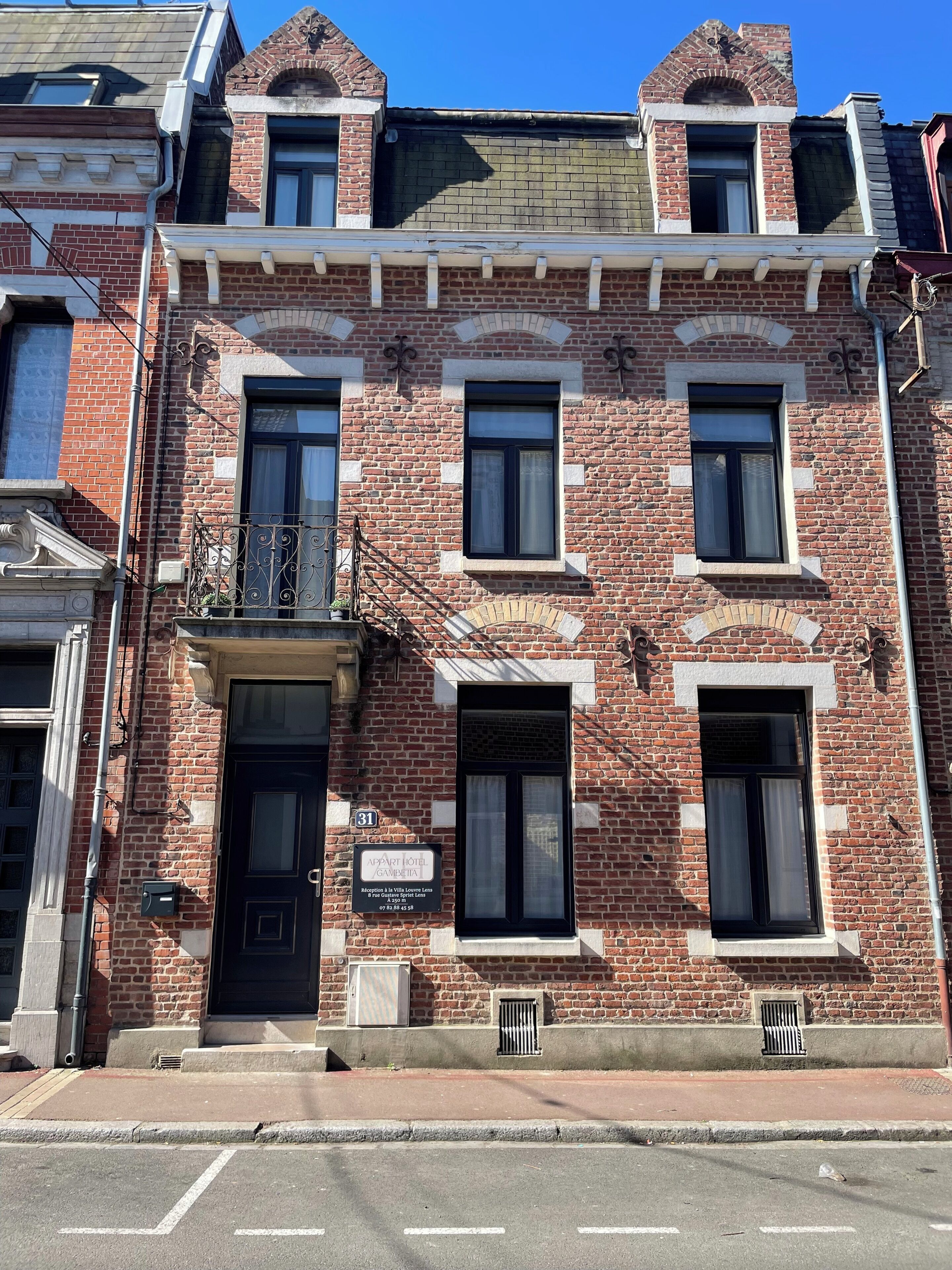 A brick building with a black door, windows, and a balcony.