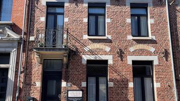 A brick building with a black door, windows, and a balcony.