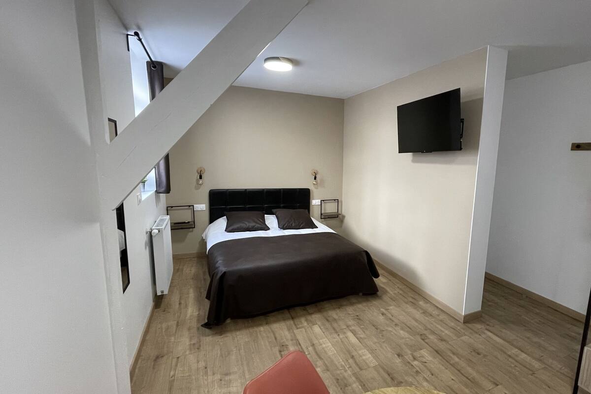 A modern hotel room with a bed, a TV mounted on the wall, and a wooden floor.