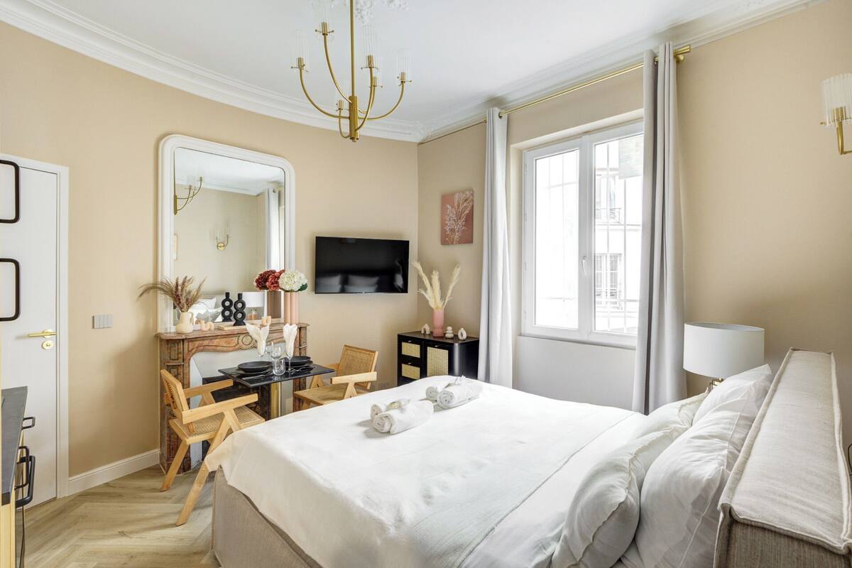 A hotel room with a large bed, a desk with chairs, a television, and a window with curtains.