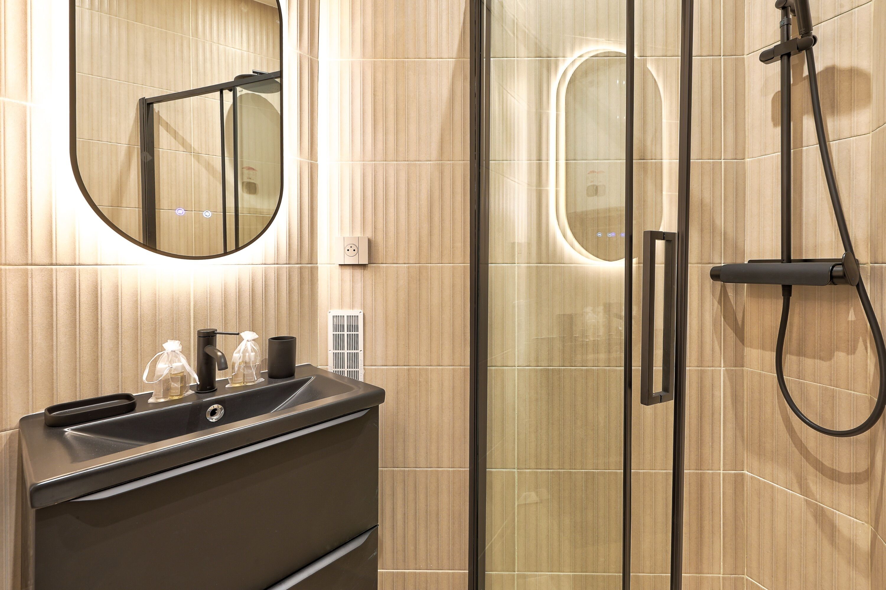 A modern bathroom with a glass-enclosed shower, a round mirror, and a dark-toned vanity with a sink.