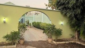 A pathway leading to a building with a green wall, potted plants, and a sign indicating room numbers 105-120. - Quarter House Hotel (Kano)
