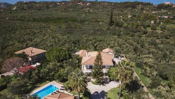 An aerial view of a residential area with two houses, a swimming pool, and surrounding greenery.