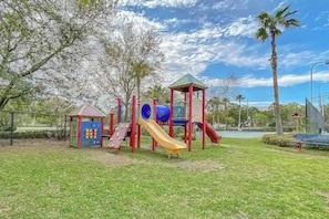 Un parque infantil con toboganes y estructuras para escalar, rodeado de césped y árboles.