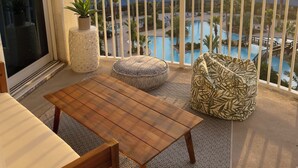 A balcony with a wooden table, two patterned cushions, and a potted plant.