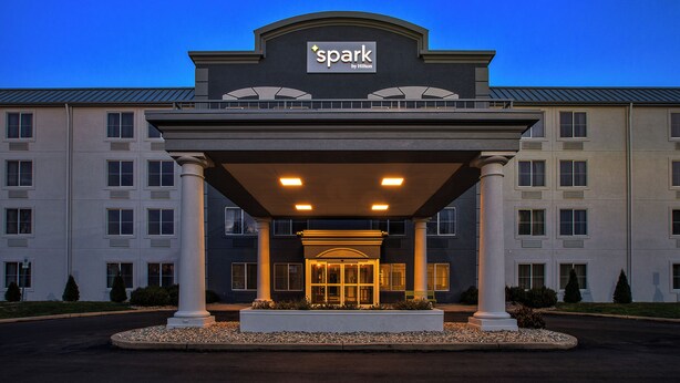 A hotel entrance with a 'Spark by Hilton' sign, a covered entrance area, and a landscaped front with a gravel area and small shrubs. - Spark By Hilton Walker Grand Rapids North (Grand Rapids)