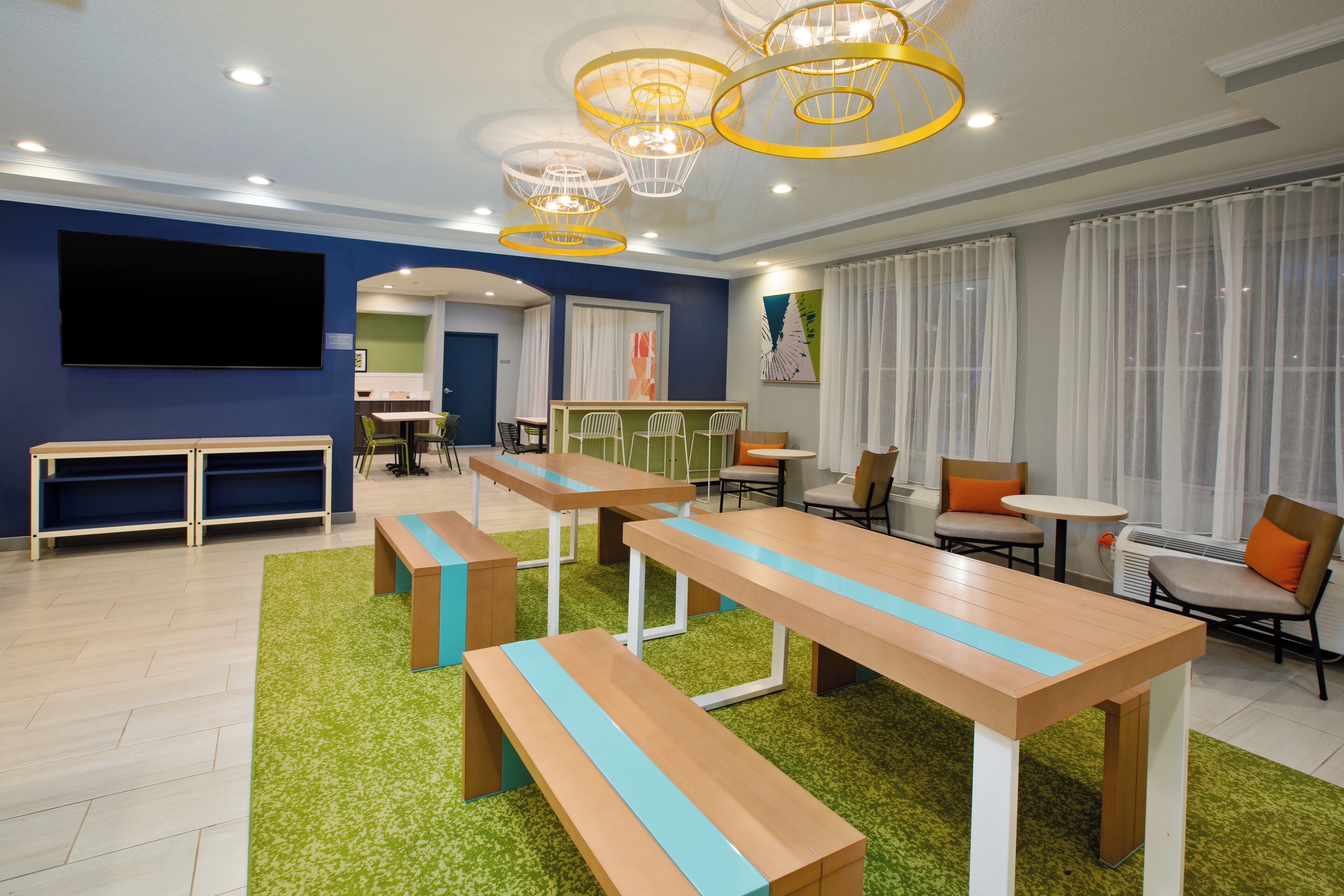 A modern meeting room with long tables, benches, and a large screen.
