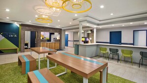 A modern indoor space with wooden tables and benches, a reception area, and a counter with chairs. - Spark By Hilton Walker Grand Rapids North (Grand Rapids)
