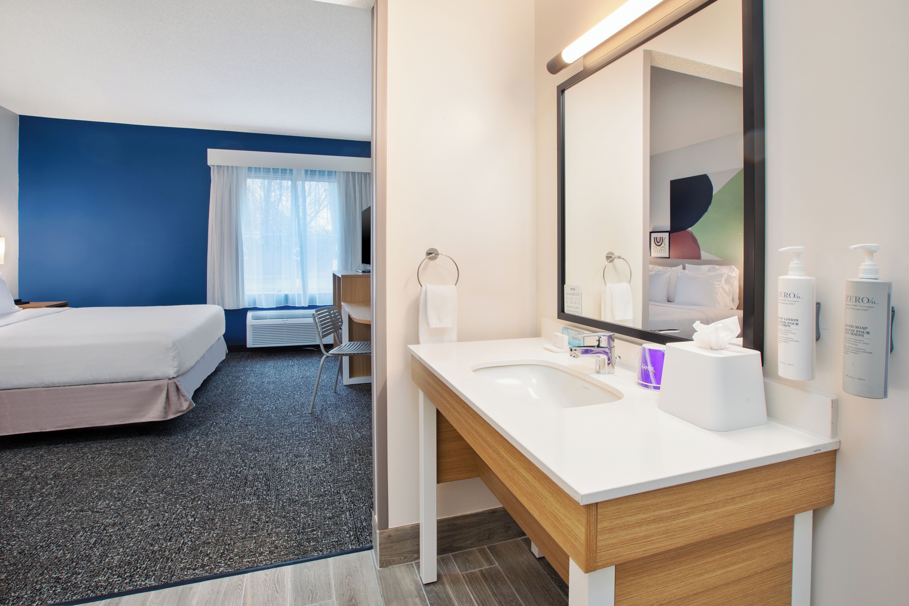 A hotel room with a bed, a bathroom with a sink and mirror, and a chair.