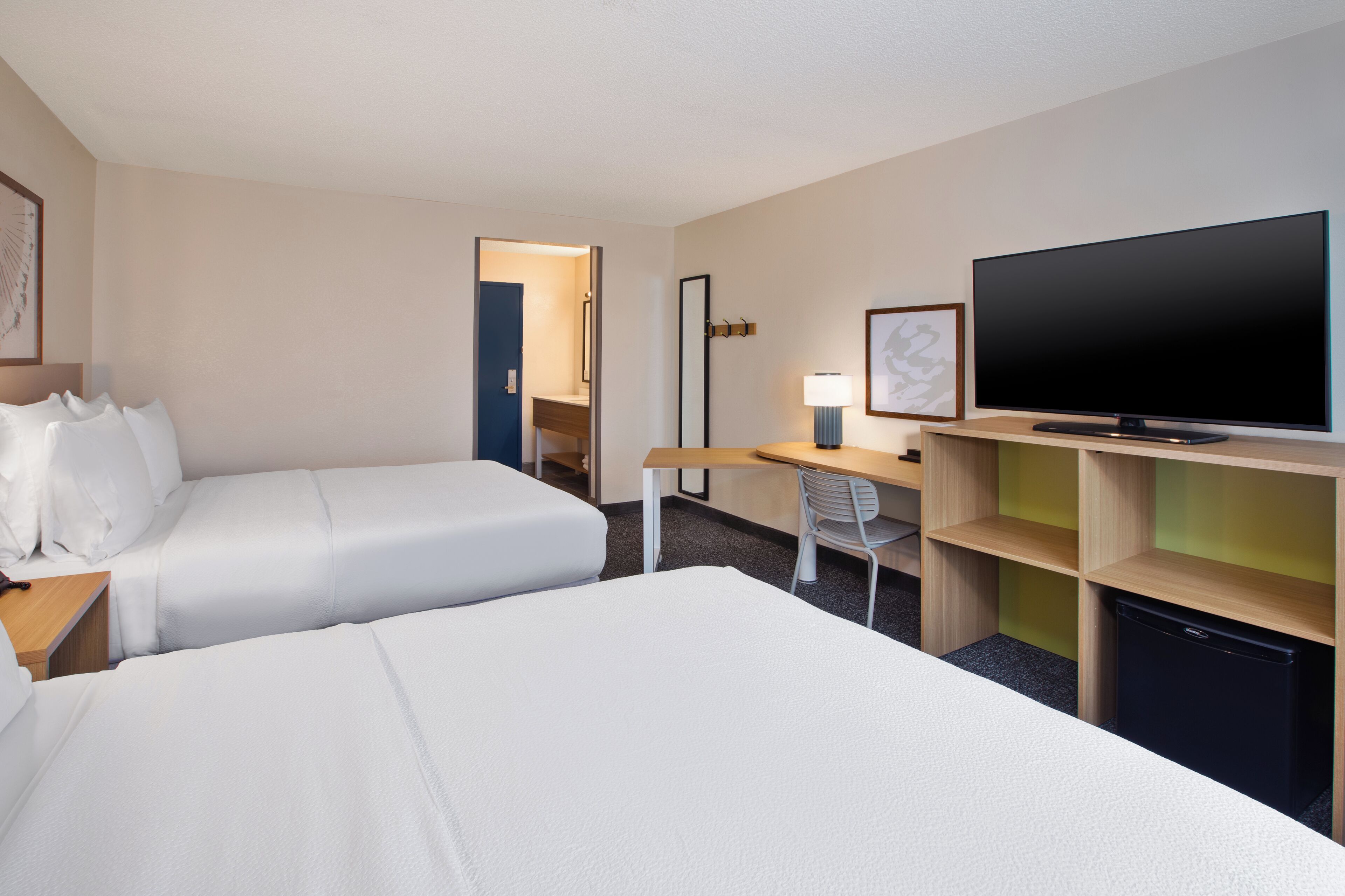 A hotel room with two beds, a desk, a television, and a small refrigerator.
