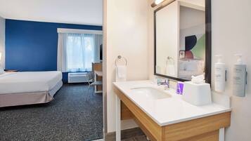 Une chambre d’hôtel avec un lit, une salle de bain comprenant un lavabo et un miroir, et une fenêtre avec des rideaux.