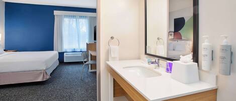 Une chambre d’hôtel avec un lit, une salle de bain comprenant un lavabo et un miroir, et une fenêtre avec des rideaux.