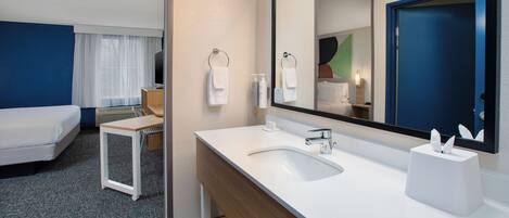 A hotel room with a bed, a bathroom with a sink and mirror, and a small table.