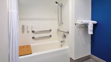 A modern bathroom with a walk-in shower, grab bars, a wooden bath mat, and a towel rack.