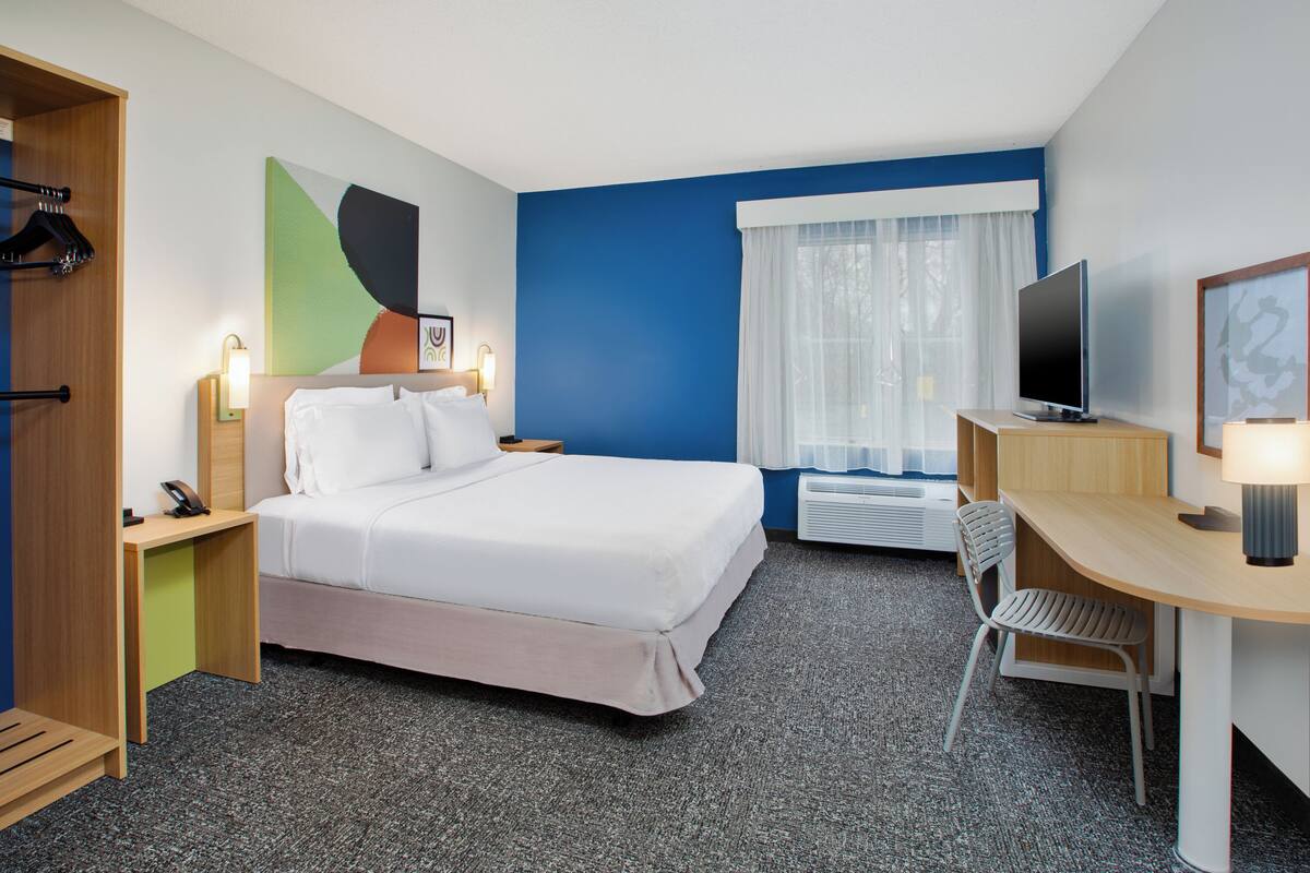 A hotel room with a bed, desk, chair, TV, and a window with curtains.
