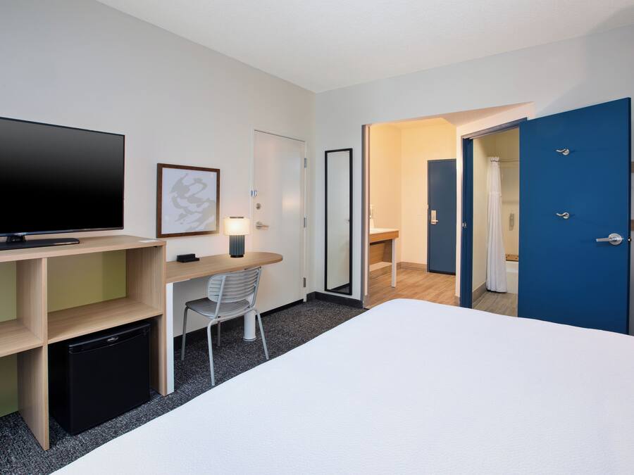 Una habitación de hotel con cama, escritorio, silla, televisión y una puerta azul.