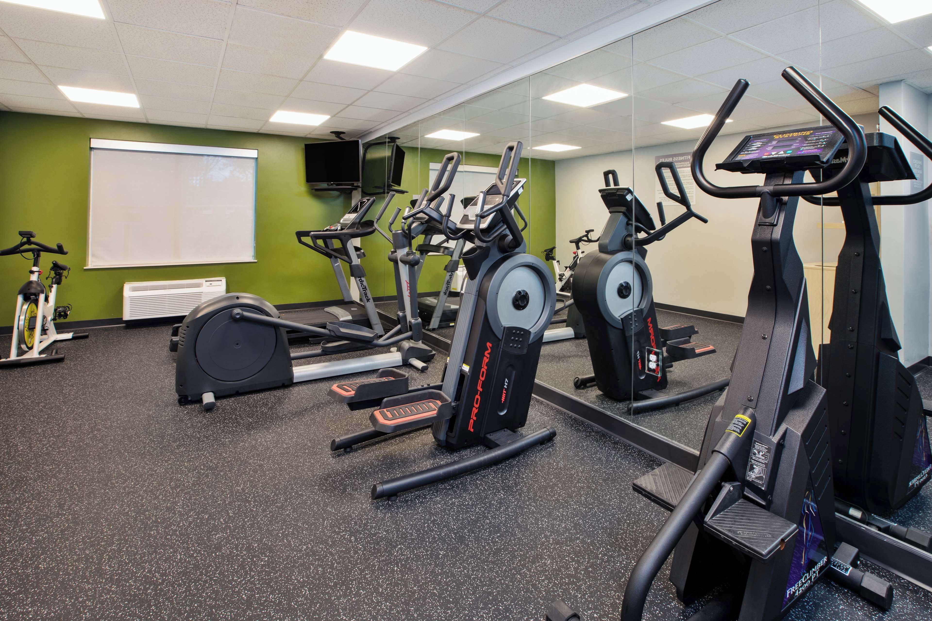 Un gimnasio con bicicletas estáticas, cintas de correr y un espejo grande.