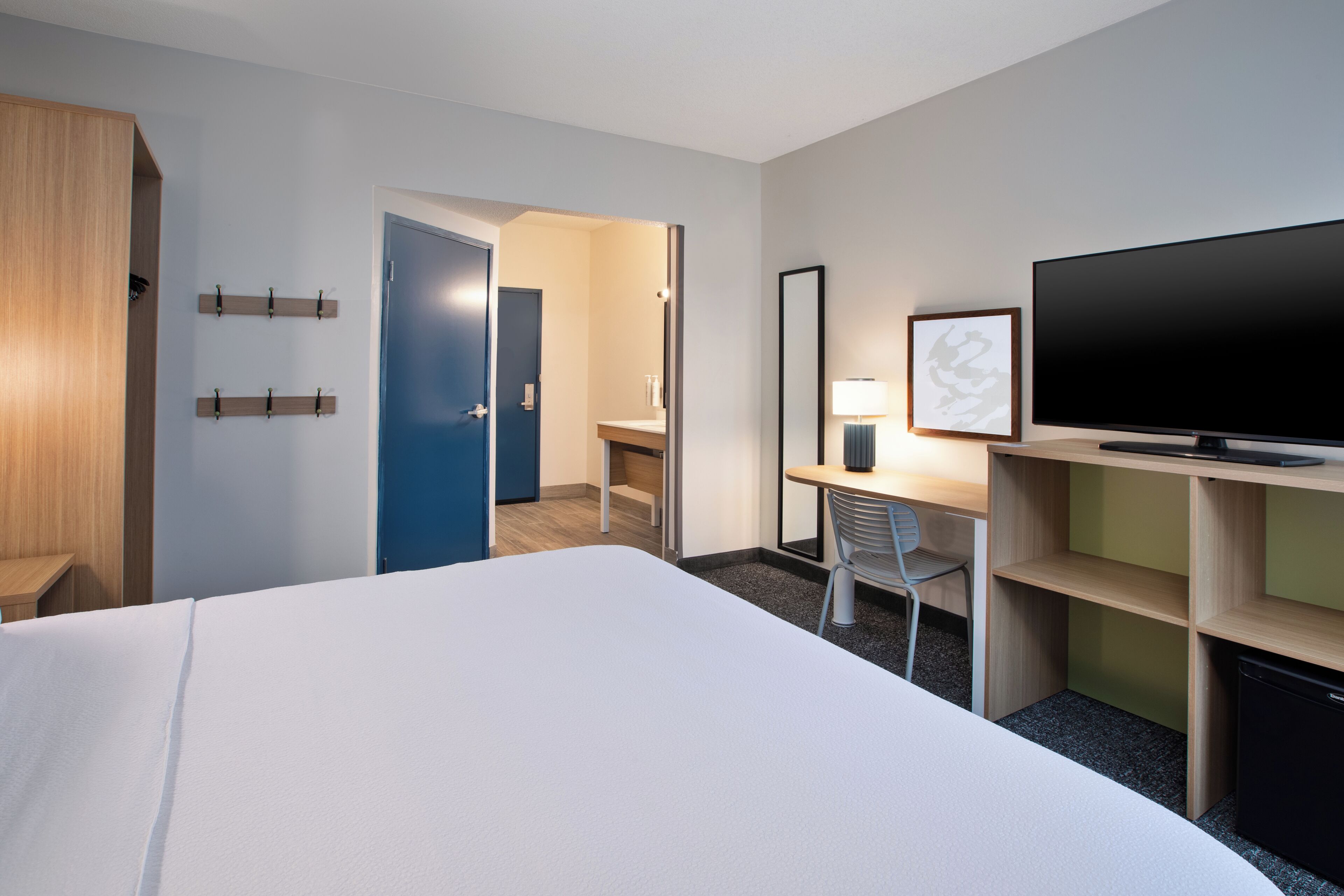 A hotel room with a large bed, a desk with a chair, a television, and a wardrobe.