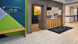 A hotel reception area with a modern design, including a wooden reception desk, a bench, and a colorful wall with the text "It only takes a spark". - Spark By Hilton Walker Grand Rapids North (Grand Rapids)