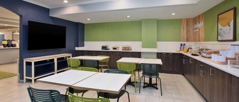 Una cocina moderna con mobiliario verde y blanco, un televisor de pantalla plana y una pared de acento de madera.