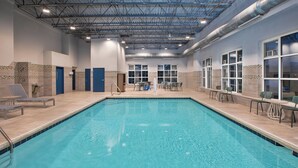An indoor swimming pool with clear water, surrounded by lounge chairs and tables, and a tiled wall with decorative patterns. - Spark By Hilton Walker Grand Rapids North (Grand Rapids)