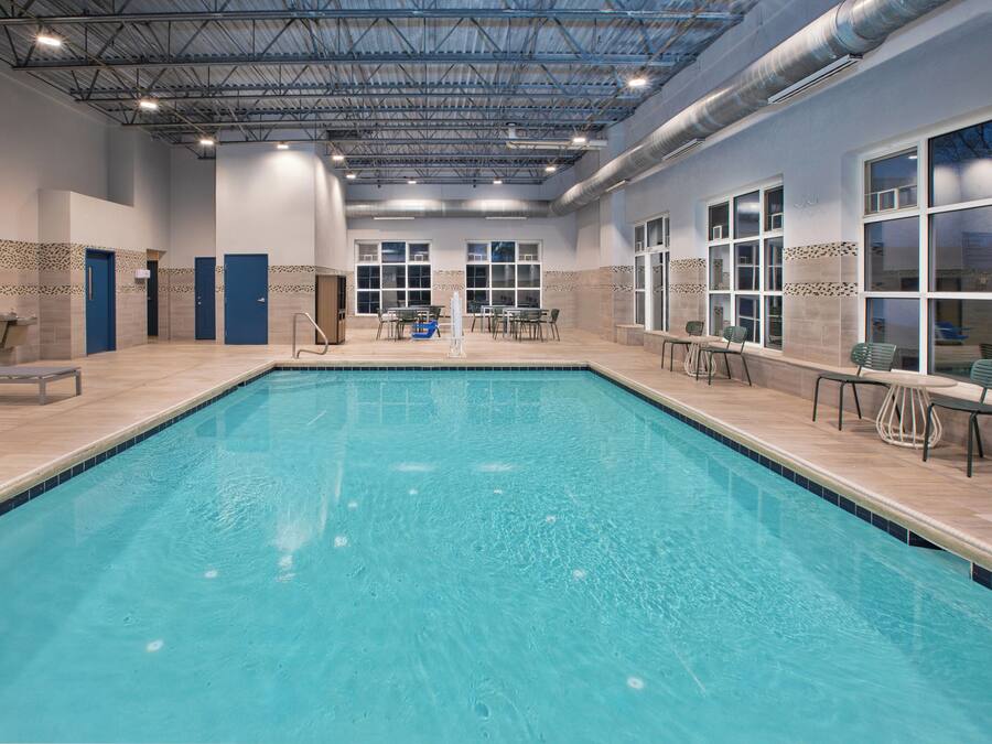 An indoor swimming pool with clear water, surrounded by lounge chairs and tables, and a tiled wall with decorative patterns.