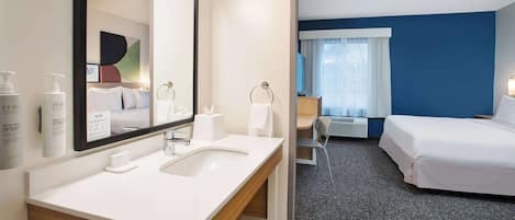 A hotel room with a large mirror, a white sink, and a bed.