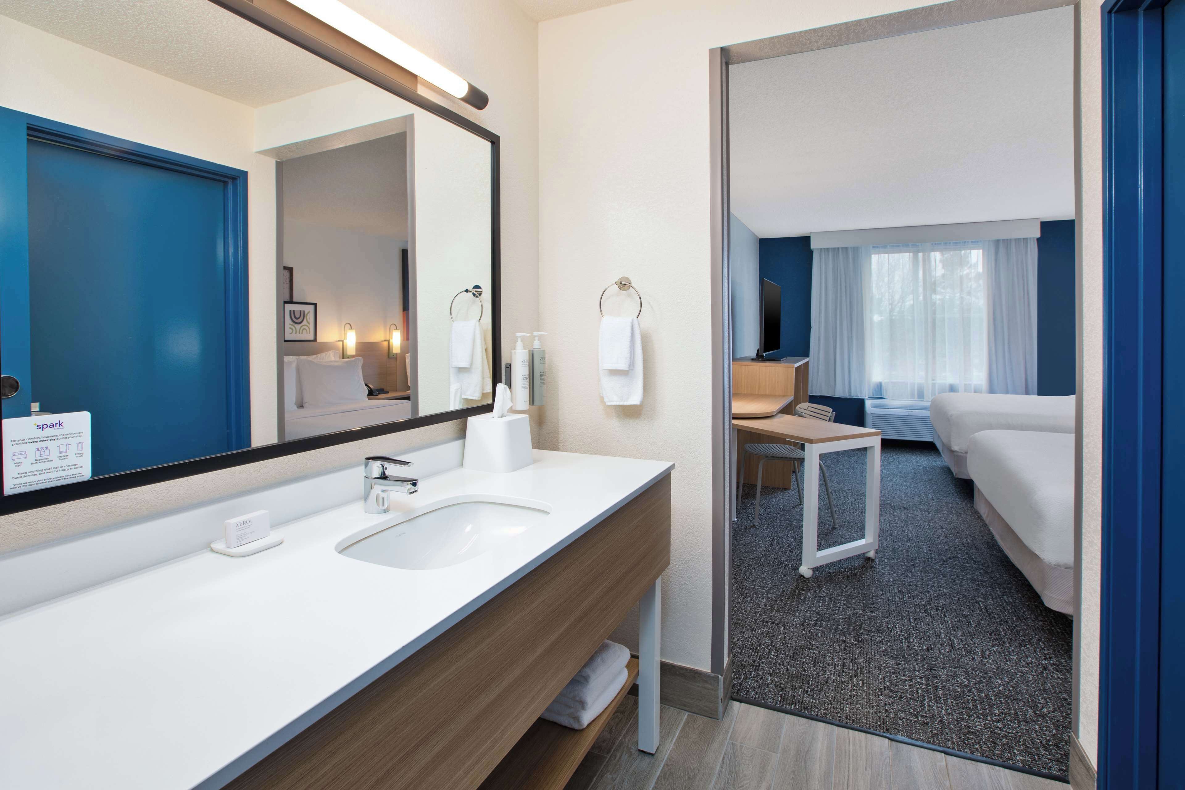A modern hotel bathroom with a large mirror, two sinks, and a shower area.