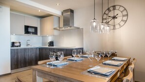 A modern kitchen with a central island, a dining area with a wooden table set for six, and a large wall clock. - Wifi, 150m from ski slopes, 2nd floor, view mountain, sauna, balcony, fireplace or stove, parking (Courchevel)