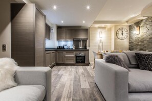 Eine moderne Küche mit Holzausstattung und einem eingebauten Ofen. Ein Essbereich mit Tisch und Stühlen sowie ein Wohnzimmer mit Sofa und Katze.