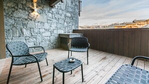 En träveranda med två stolar och ett litet bord, en stenmur och en utsikt över berg i bakgrunden.