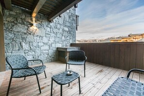 Eine Holzterrasse mit zwei Stühlen und einem kleinen Tisch, eine Steinmauer und ein Blick auf die Berge im Hintergrund.