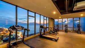Un gimnasio con amplios ventanales que dan a un paisaje urbano, equipado con cintas de correr y bicicletas estáticas.
