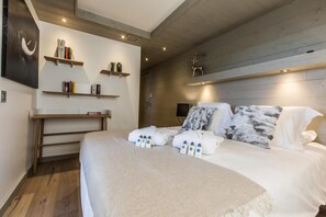 A modern hotel room with a large bed, wooden headboard, and built-in shelves with books.