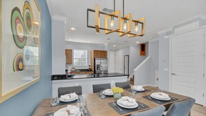 Un moderno comedor con una mesa de madera dispuesta para cuatro, una cocina al fondo y una escalera que sube a otro nivel.