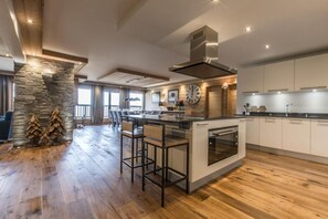 A modern kitchen with a central island, wooden flooring, a stone accent wall, and a large window providing natural light.