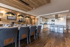 A modern kitchen with wooden flooring, a dining area with grey upholstered chairs, and pendant lighting.