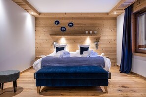 A modern bedroom with a wooden ceiling, a large bed with blue bedding, and a small round table. - Wifi, 150m from ski slopes, 3rd floor, view mountain, sauna, terrace, balcony, fireplace or stove (Courchevel)