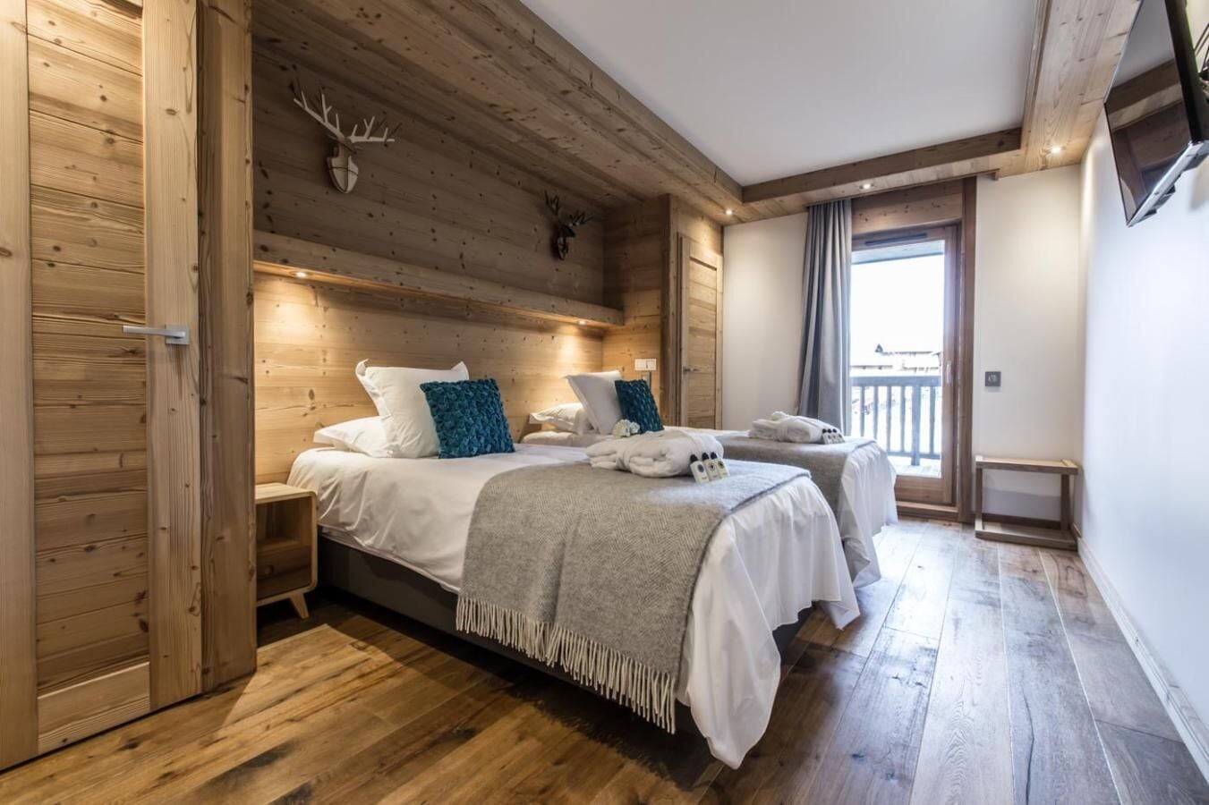 A wooden cabin-style bedroom with two beds, a balcony, and a wooden ceiling.
