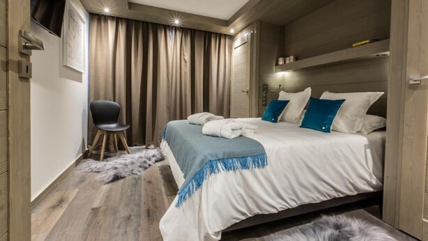 Una habitación de hotel moderna con una cama grande, una silla, una alfombra de piel y una lámpara de techo.