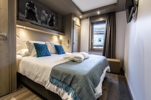 A modern hotel room with a large bed, a headboard with artwork, a bedside table, and a window with curtains.