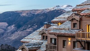 Un edificio de varios pisos con techo inclinado, balcones de madera y montañas al fondo.